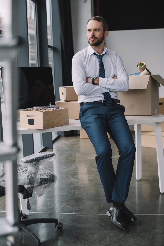 businessman with crossed arms sitting on table and looking away in new office during relocation