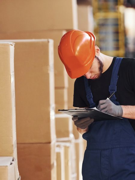 Storage worker in uniform and notepad in hands checks production